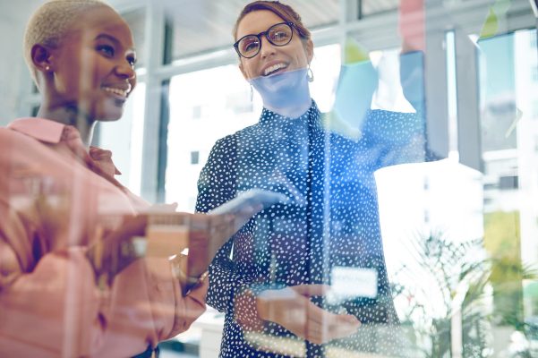 Shot of two businesswomen brainstorming with notes on a glass wall in an office.