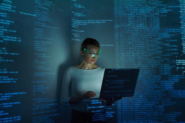 Confident woman in futuristic glasses using computer against dark background